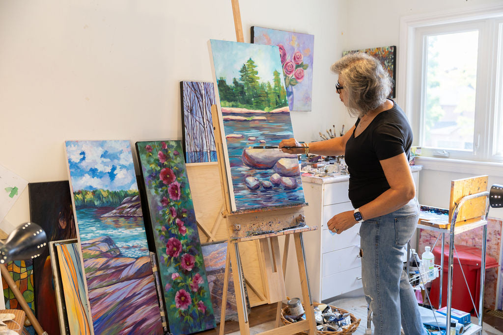 Person painting in a studio with various artworks on easels.