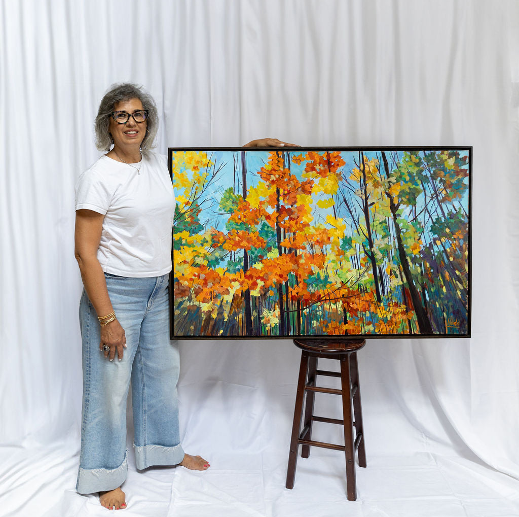 Person holding a painting of a forest scene with trees in autumn colors against a white curtain.