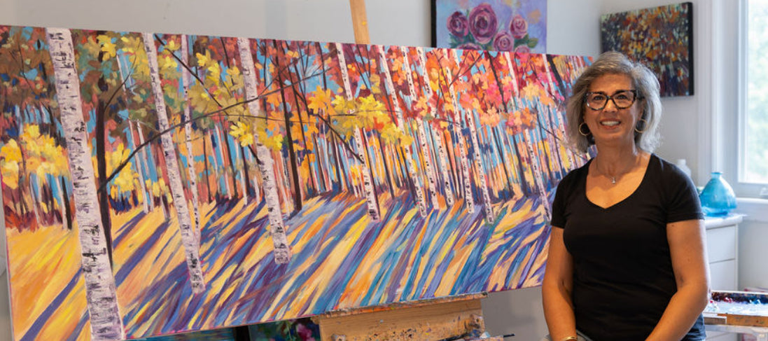 Artist standing next to a large abstract painting of a forest scene